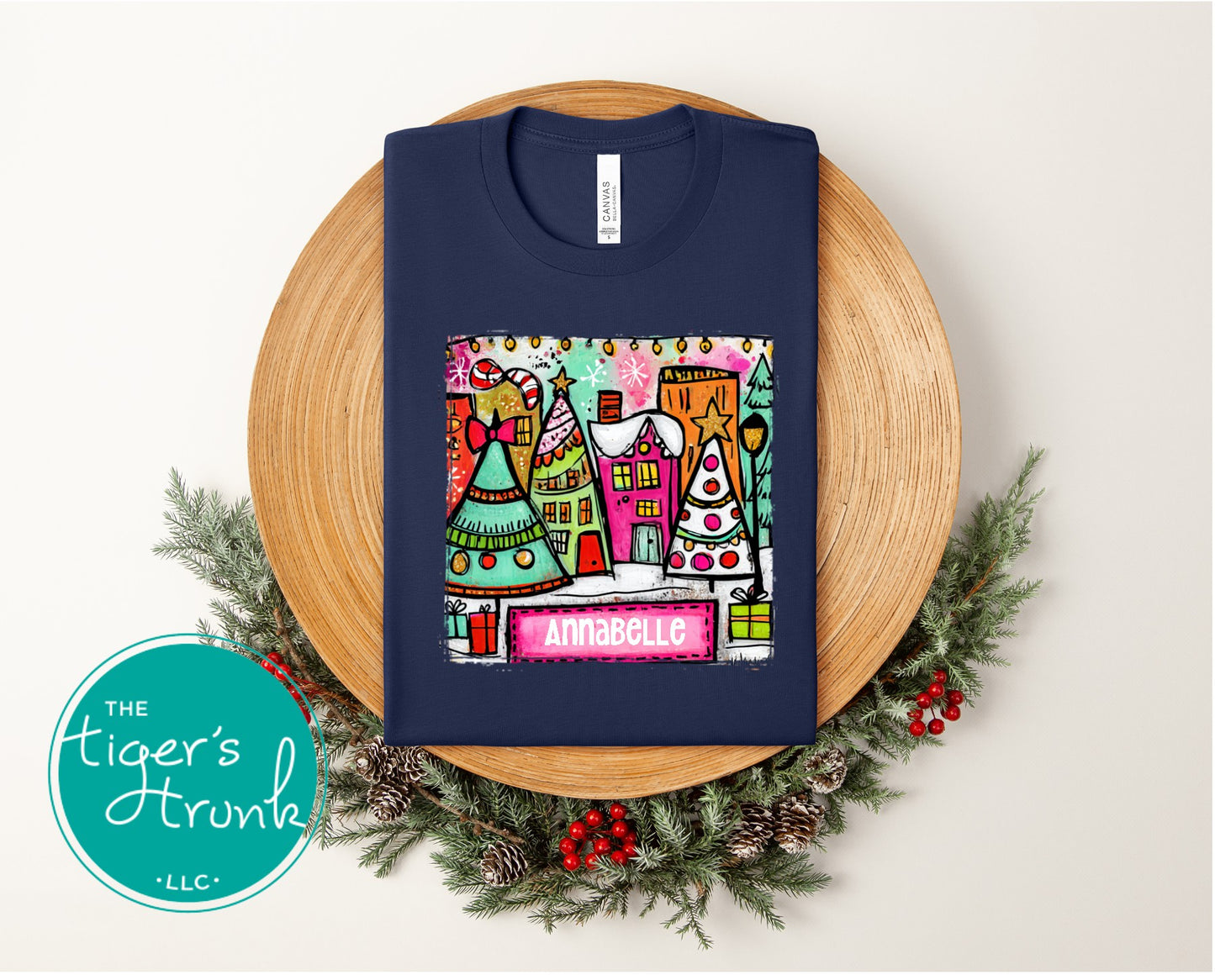 Navy blue sweatshirt with colorful Christmas village design on a wooden plate with greenery