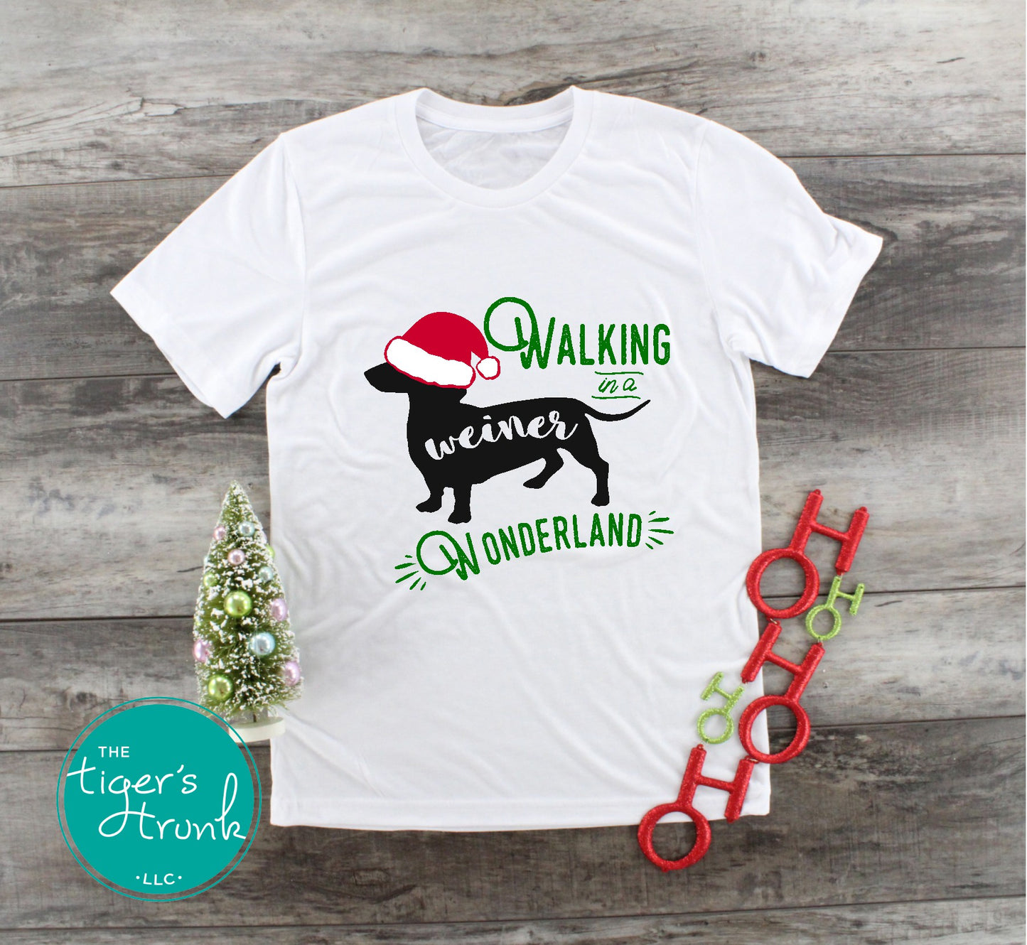 White t-shirt with Christmas-themed design featuring a dog and text, displayed on a wooden surface.