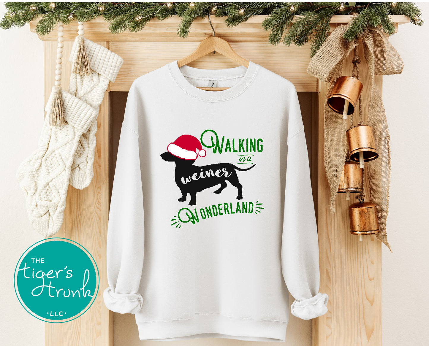 White sweatshirt with Christmas-themed design hanging on a wooden mantel with decorative items.