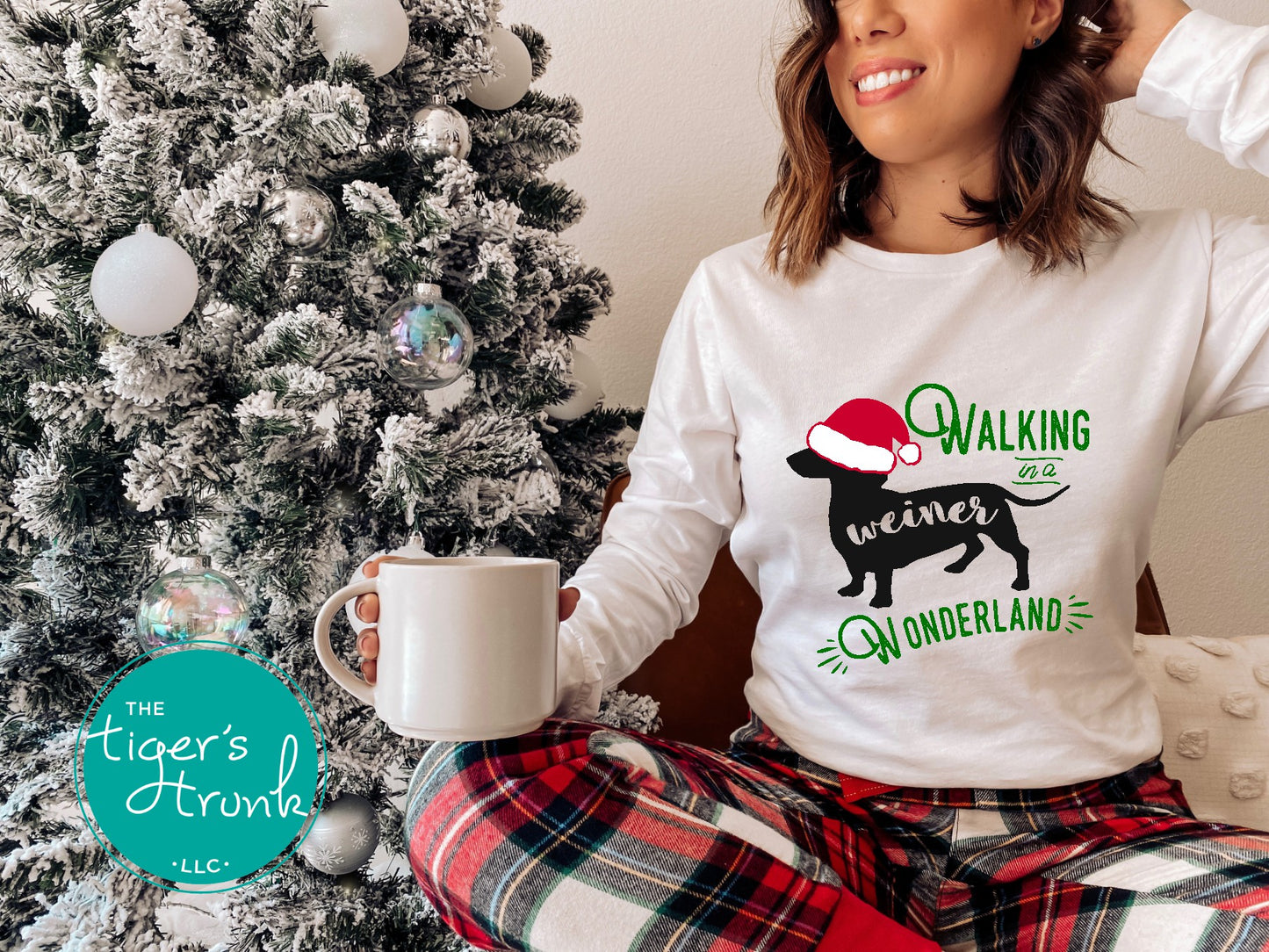 Person wearing a white sweatshirt with a Christmas design, holding a mug in front of a decorated Christmas tree.