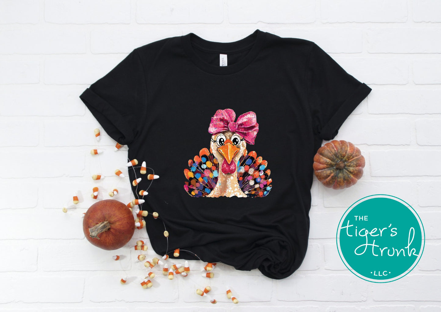 Black t-shirt with a turkey graphic and bow, surrounded by pumpkins and corn on a white background.