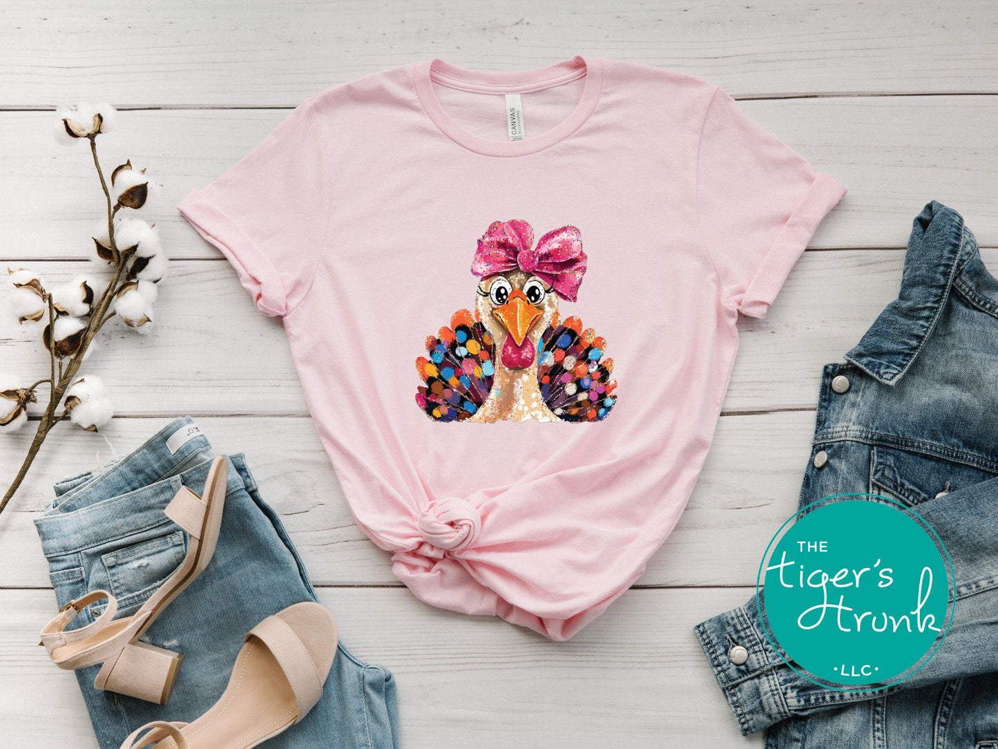 Pink t-shirt with a colorful turkey design and bow, paired with denim jeans and heels on a light wooden surface.