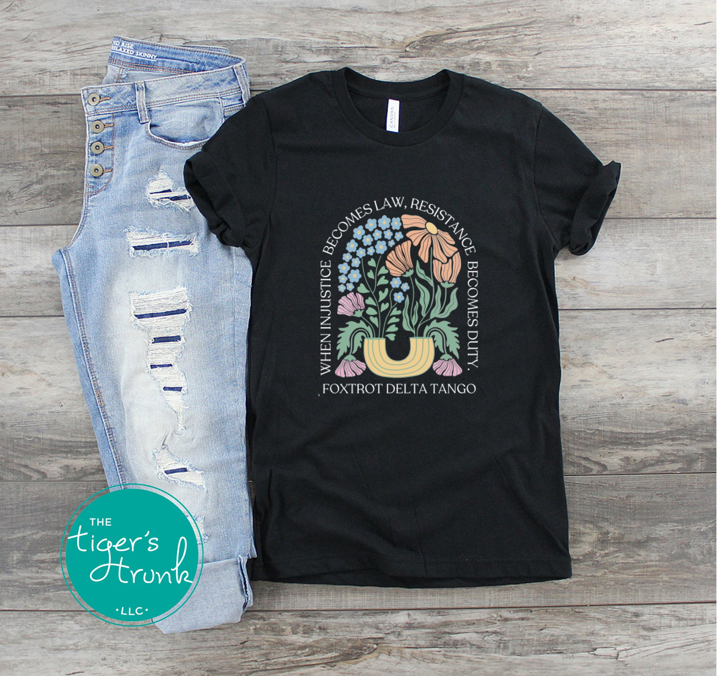 Black t-shirt with graphic design and text, paired with light blue jeans on a wooden surface, branded 'The Tiger's Trunk'.