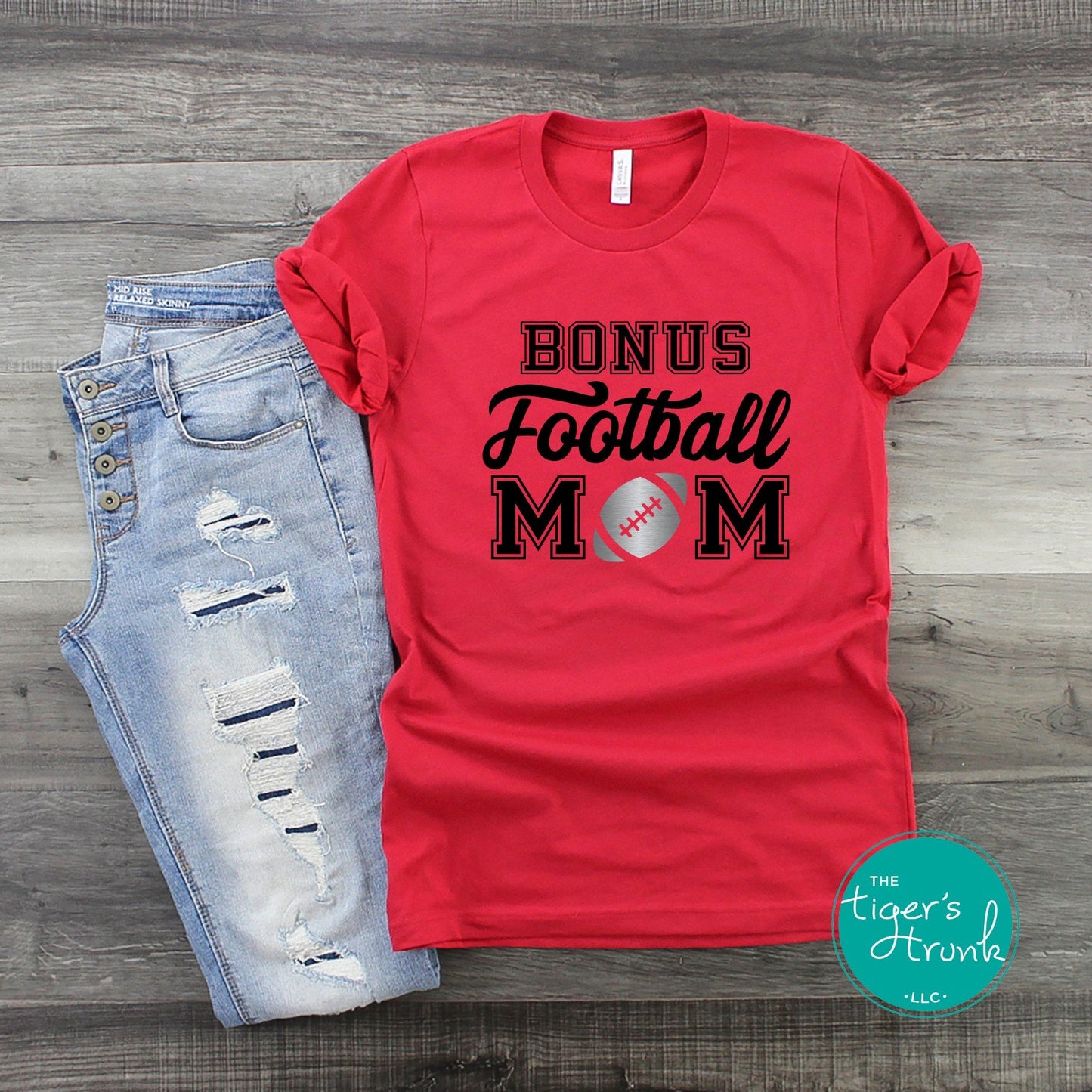 Red Bonus Football Mom shirt with personalized team colors displayed next to distressed jeans on wood background.