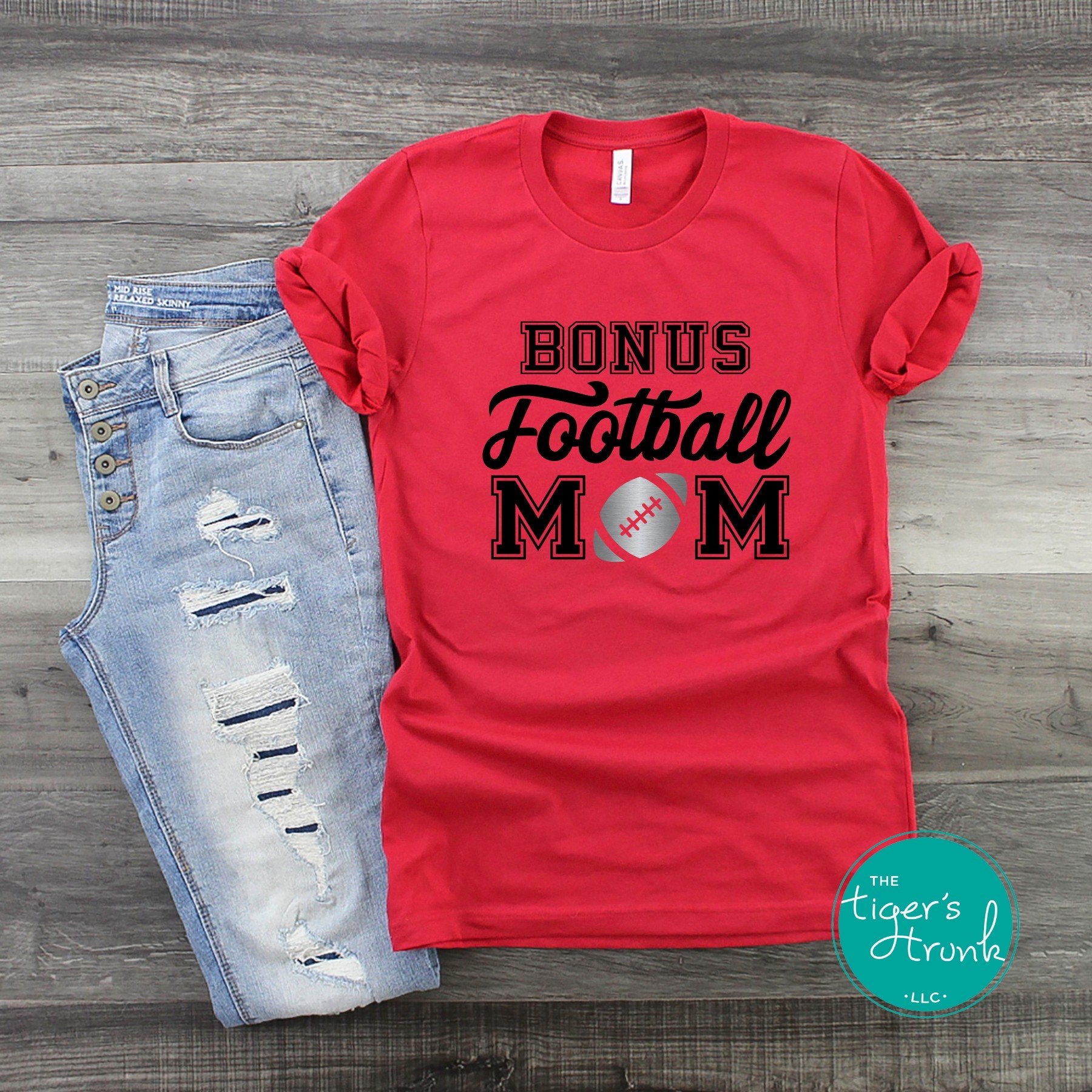 Red Bonus Football Mom shirt with personalized team colors displayed next to distressed jeans on wood background.