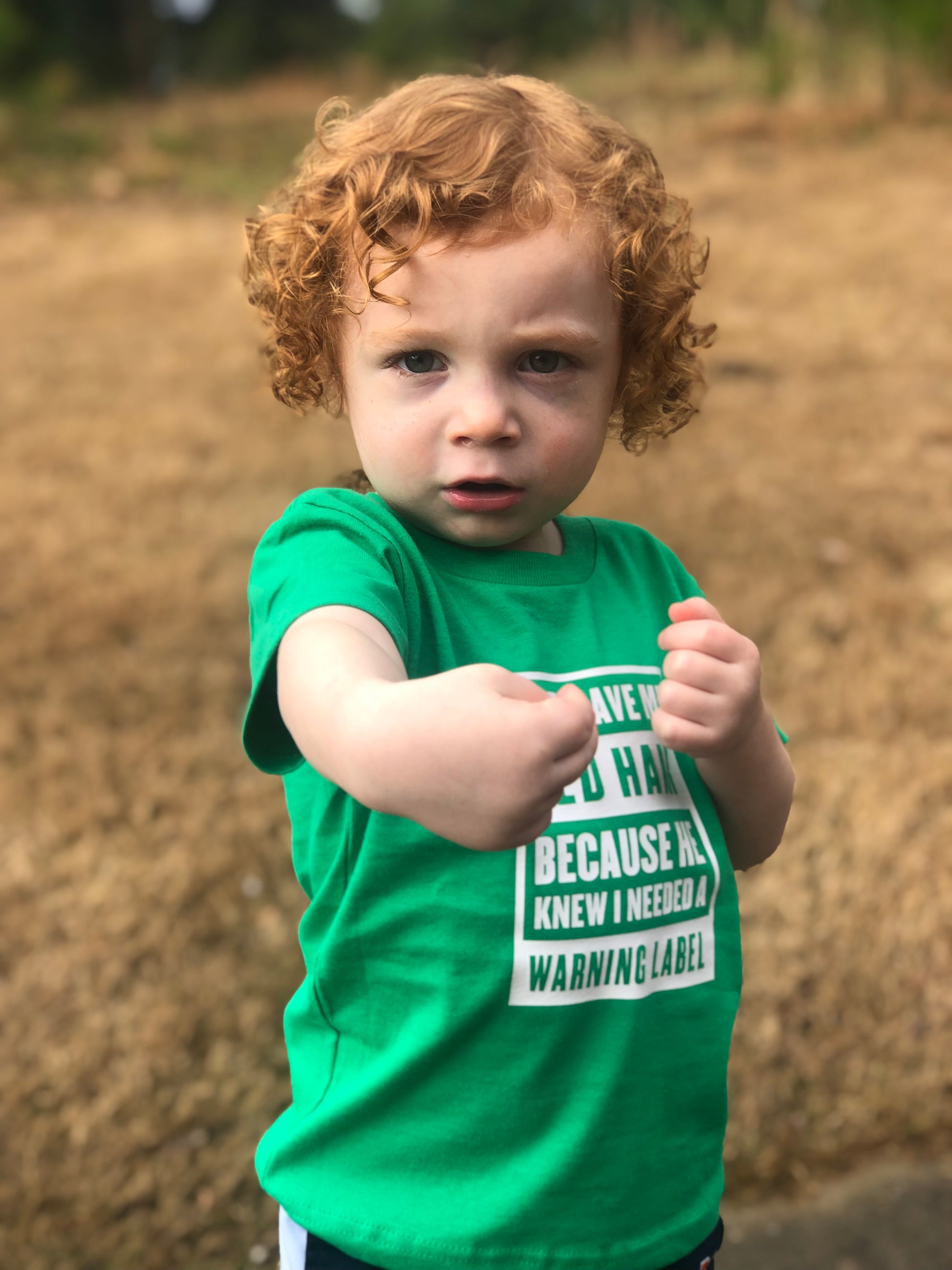 oung child posing in green St. Patrick’s Day red hair warning label shirt.