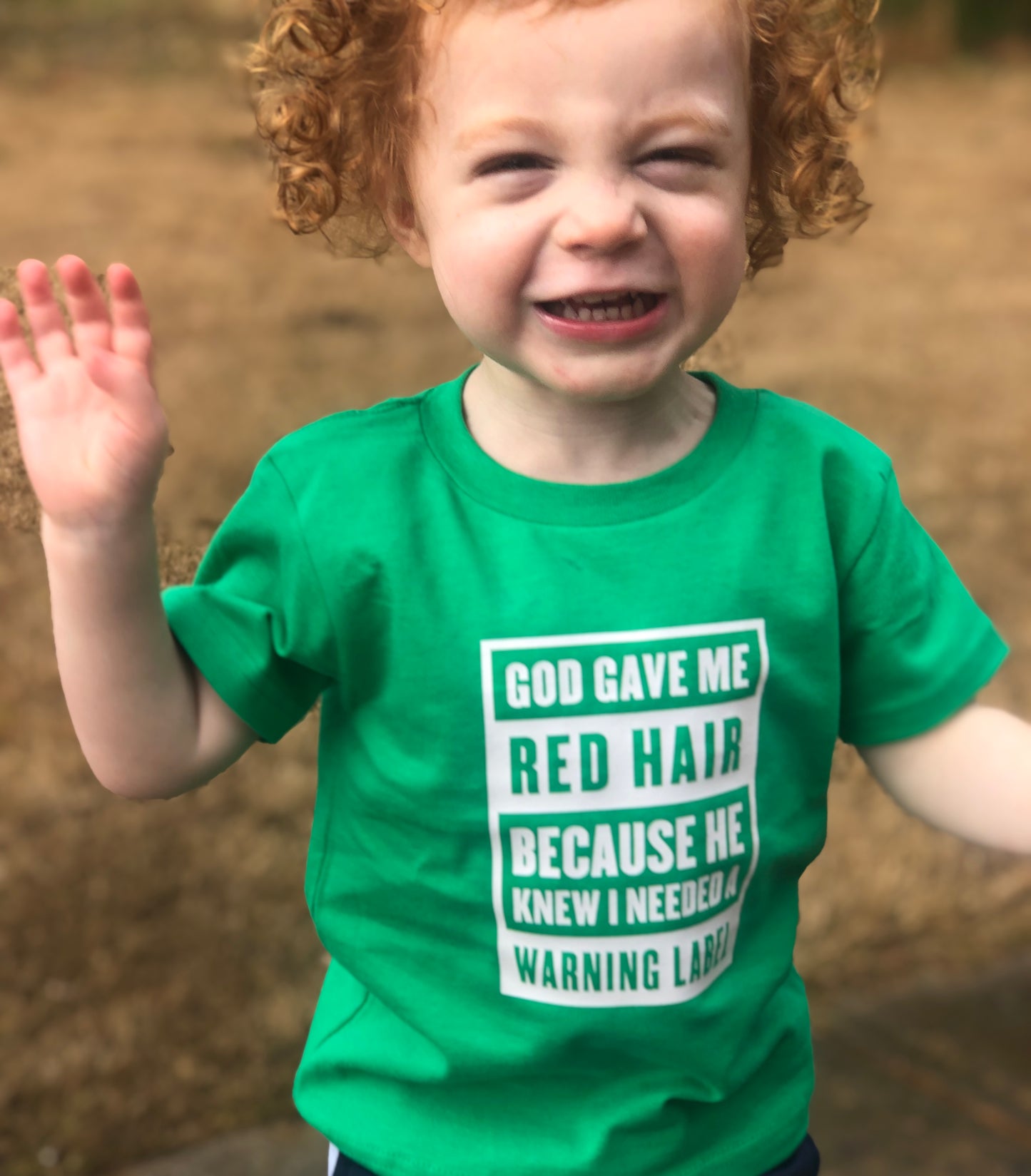 Smiling child wearing green St. Patrick’s Day red hair warning label shirt.